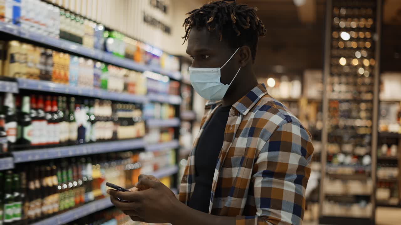 Uomo attraente con smartphone cammina nel negozio, controllando la lista della spesa.
