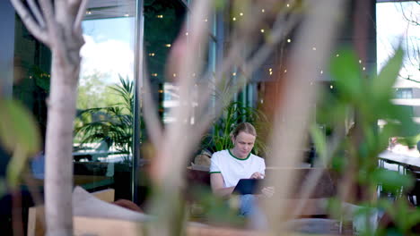 professional working remotely while sitting in lush garden like outdoor cafe, concentrating on laptop with natural light softly filtering through surrounding greenery and foliage