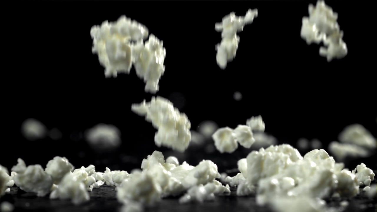 Cottage cheese-biter som faller ned på en svart overflate i sakte film