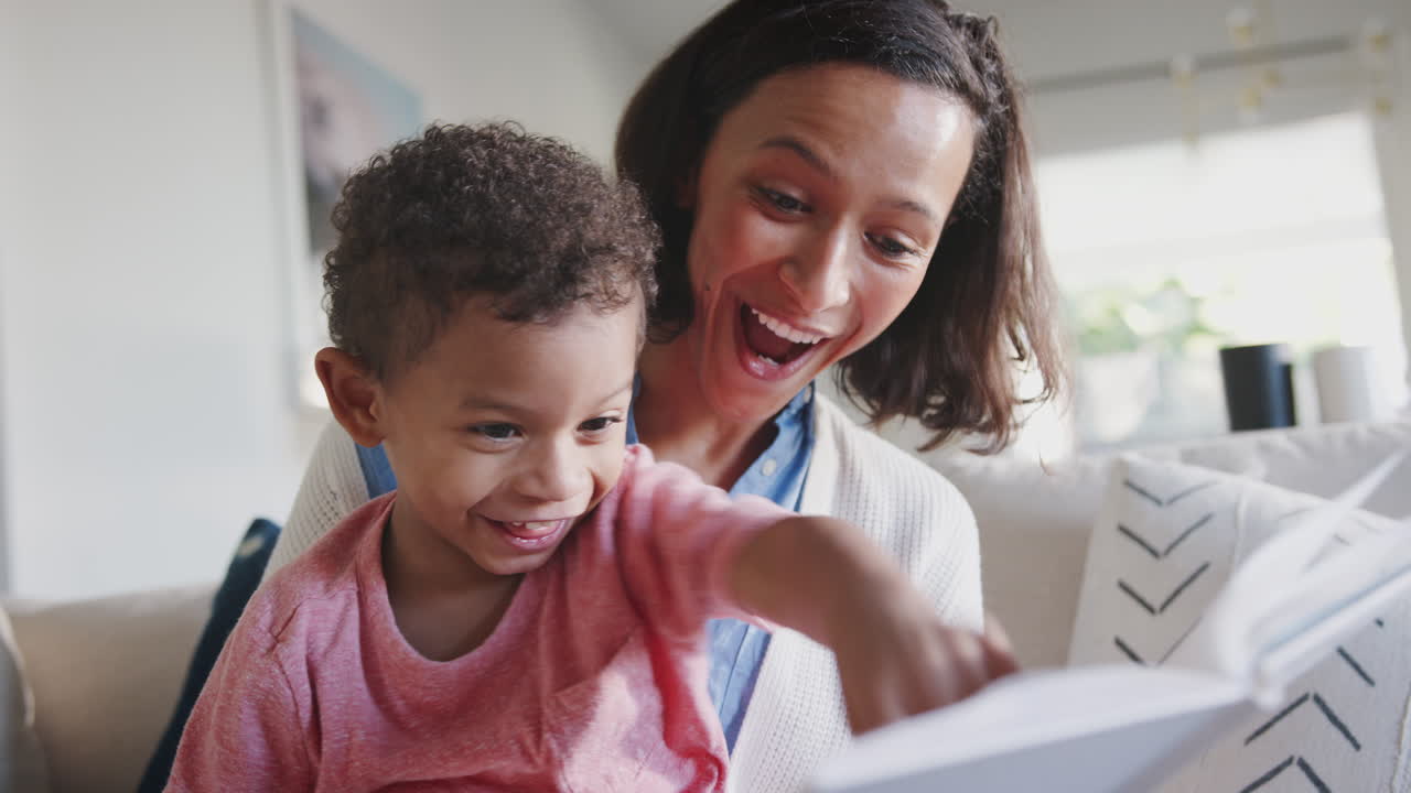 African American mum sitting on sofa reading to her toddler son, low angle, close up