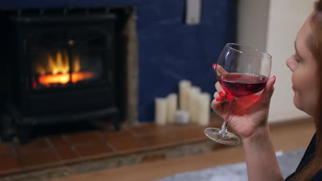 close up of a woman with a glass of wine sitting in front of a fireplace watching a fire in a living room