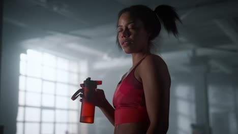 tired sportswoman with water bottle standing in gym. woman taking break