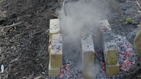 shoveling hot coals onto bricks on a backyard oven