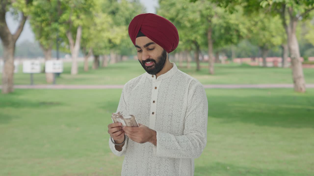 Uomo indiano Sikh felice che conta soldi nel parco.