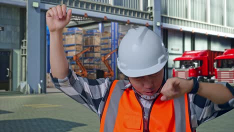Close Up Of Asian Male Engineer With Safety Helmet Screaming Goal And Dancing Celebrating , Outside of Logistics Distributions Warehouse