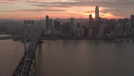 Kreisende-Aufnahme-Der-Bay-Bridge-Mit-San-Francisco-City-Im-Hintergrund-Bei-Sonnenuntergang