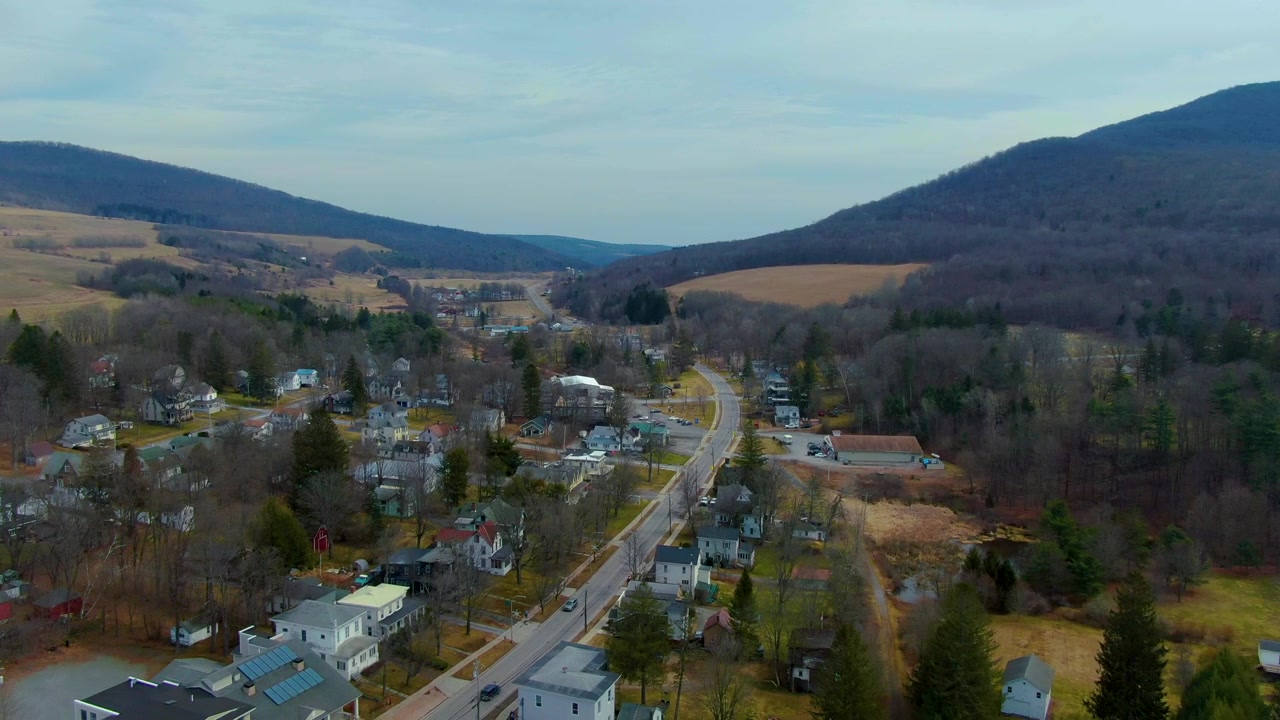 Toma de dron descendiendo sobre una comunidad rural con carreteras sinuosas y paisaje montañoso durante el día en Stanford, Nueva York.