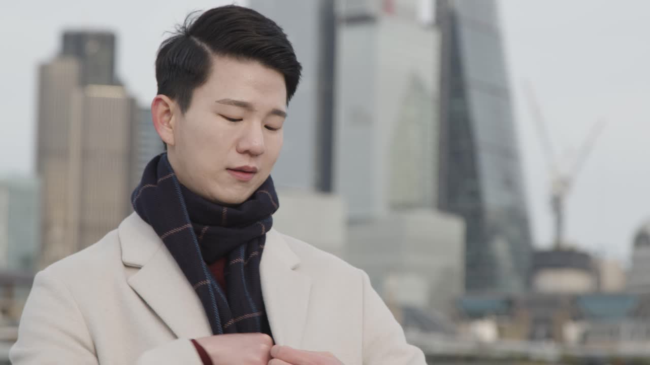 런던 시내 스카이라인을 배경으로 휴대전화로 전화를 받는 젊은 아시아 사업가