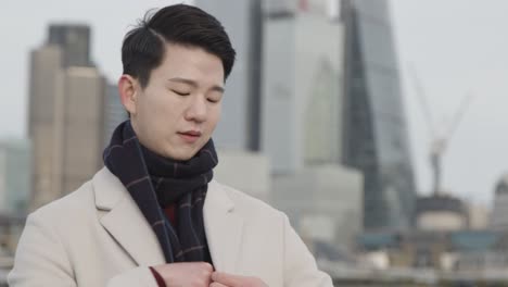 young asian businessman answering call on mobile phone with london city skyline in background