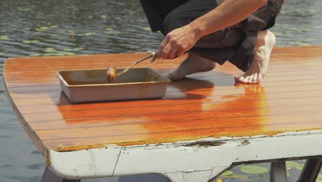 man walks into shot and begins painting roof of wooden boat cabin