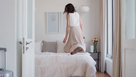 happy woman jumping on bed in hotel room having fun enjoying vacation lifestyle celebrating freedom