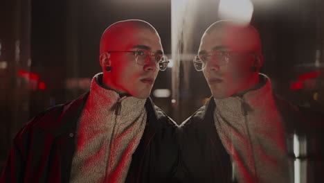 man looking at his reflection in a window at night