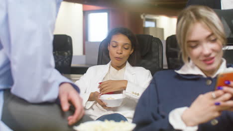 girl eating popcorn and drinking soft drink while sitting at the office with her colleagues during a party