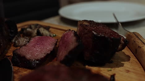 Delicious-thick-juicy-cooked-red-steaks-and-sliced-on-wooden-chopping-block,-close-up-rack-focus