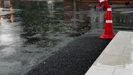 close-up of rain falling on the road, creating artistic ripples and patterns around an orange cone