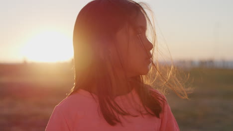 Primer-Plano-Retrato-Hermosa-Niña-Que-Parece-Tranquila-Disfrutando-De-Un-Día-De-Verano-Sin-Preocupaciones-En-El-Parque-Atardecer-Viento-Soplando-Cabello-Infancia-Pacífica