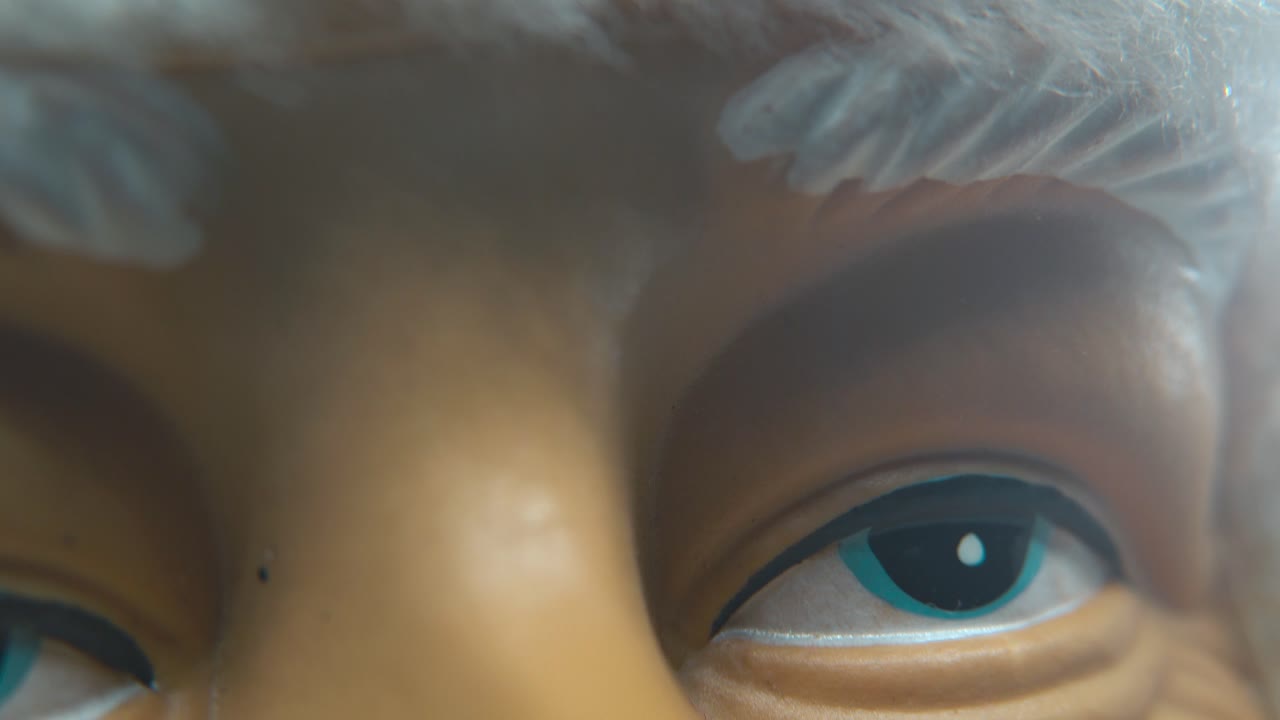 X-mas plastic Santa Claus face in a red hat, big white beard and eyebrows, blue eyes, Christmas decoration, traditional holiday new year decor, cinematic lighting, creative slow macro tilt down shot