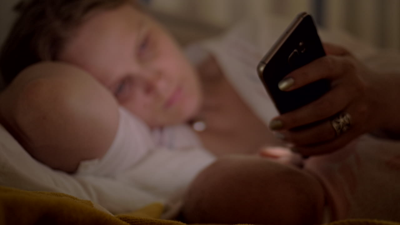 Woman using mobile when breastfeeding baby at night