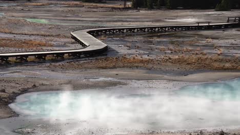 steam billows from a pool near a boardwalk in yellowstone national park