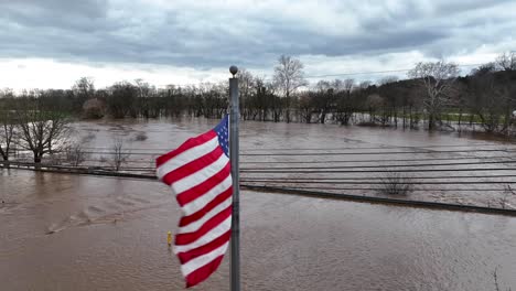 American-flag-above-brown-murky-water-from-flooded-river-in-park