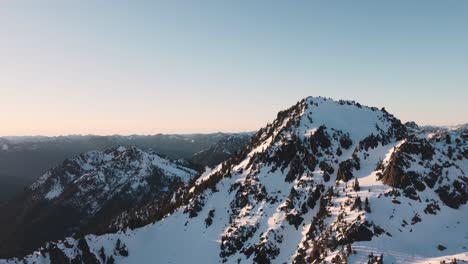 an orbiting drone shot of a snowy peak in the olympic mountains taken from just outside the national park at sunset