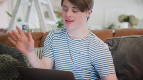 young downs syndrome man sitting on sofa watching laptop at home and dancing