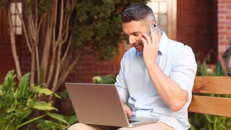 profesor feliz sentado en un banco usando una computadora portátil y hablando por teléfono