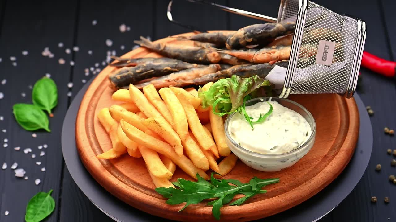 Fresh fish served with fries and sauce on a wooden plate in a restaurant. A plate holds fried fish and golden fries, accompanied by a bowl of sauce and greens