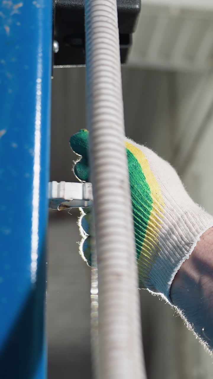 Close-up of mechanic's hairy hand wearing a glove adjusting lift mechanism in garage, blue uniform sleeve visible with brick wall background, professional automotive maintenance