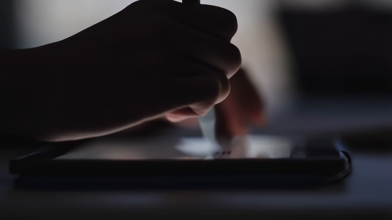 Una mano che usa uno stilo su uno smartphone in un ambiente buio