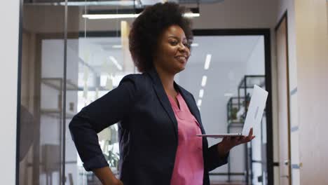 Portrait-of-african-american-woman-smiling-while-using-laptop-at-office