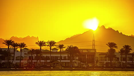 bright orange sun rising behind the mountain during sunsrise with oceanfront buildings in the foreground