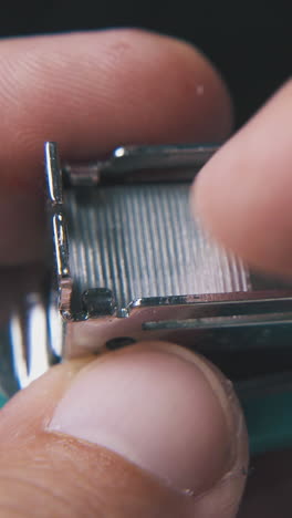 young man opens small turquoise stapler to put in metal clips on dark background extreme close view