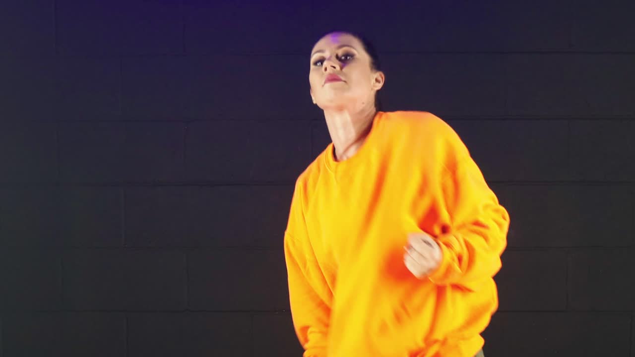 atractiva mujer joven con blusa naranja bailando hip hop de estilo libre moderno en un estudio, vista de primer plano