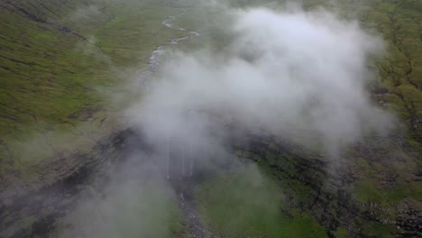 River-flowing-into-large-Fossá-Waterfall-in-Faroe-Islands,-aerial-misty-reveal