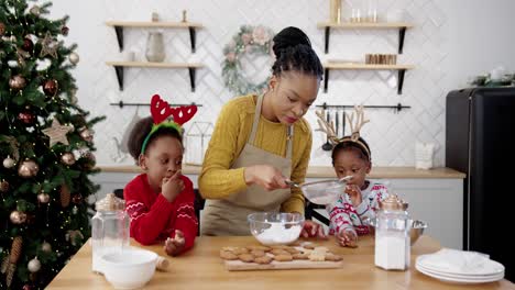 Happy-Family-With-Little-Cute-Kids-On-Christmas-Standing-At-Table-In-Kitchen-And-Decorate-Homemade-Baked-Xmas-Gingerbread-Cookies-New-Year-Preparations,-Winter-Season-Holidays-Concept