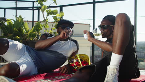 front view of gays lying on rooftop terrace and clinking glasses