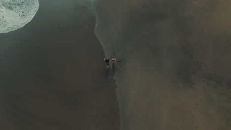 4k aerial two people walking on black sand drone overhead shot