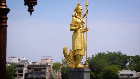 golden shiva statue at sursagar lake in vadodara, gujarat, india. spiritual landmark with clear sky and urban cityscape in background. best for religion, travel and indian culture themes.