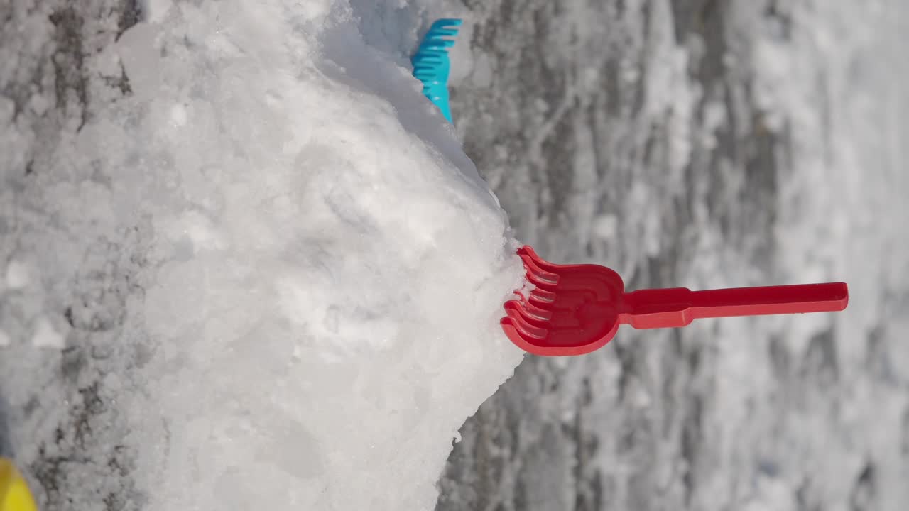 A red plastic rake in a pile of snow with another toy in the background