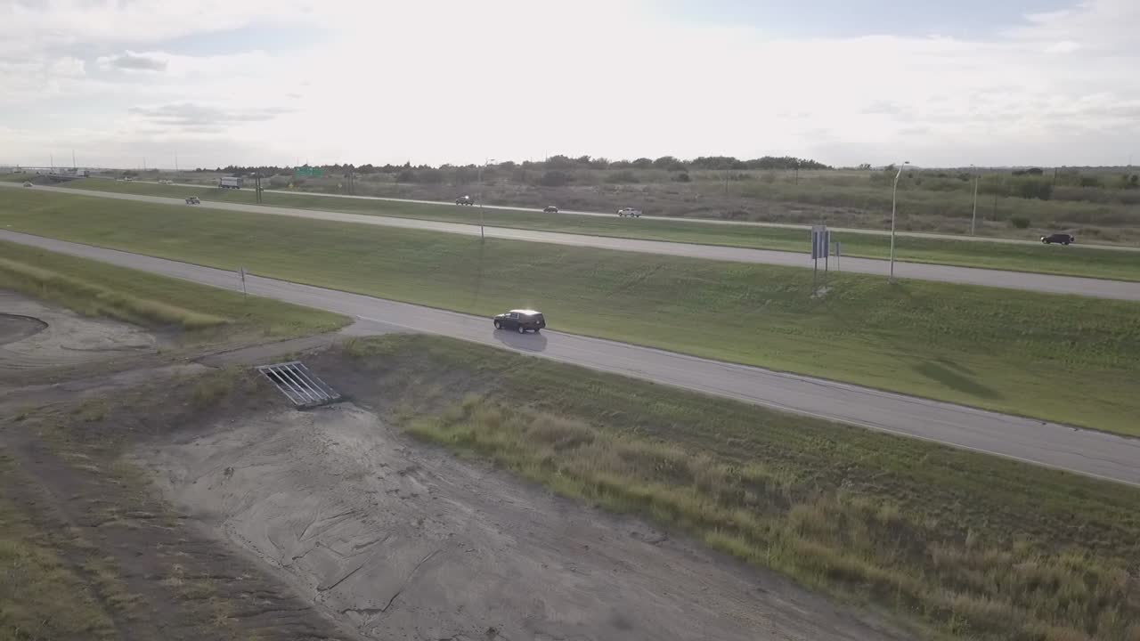 Aerial tracking vehicle driving along rural Texas interstate traffic on dusty country road