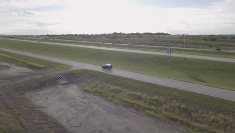 Aerial-tracking-vehicle-driving-along-rural-Texas-interstate-traffic-on-dusty-country-road