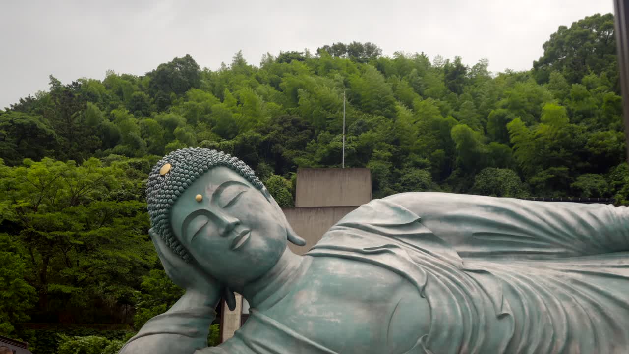 el viento sopla lentamente la hoja del árbol detrás de la estatua gigante de bronce nanzoin daibutsu fukuoka japón día nublado