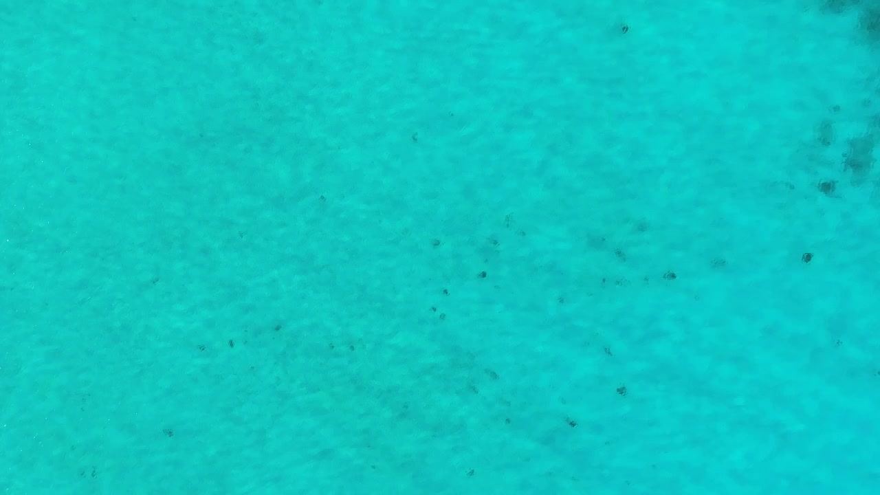 Drone descends to sandy clear caribbean ocean water, sunlight ripples dance