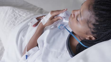 african american female patient with oxygen mask lying in bed in hospital room, slow motion