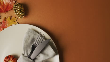 video of plate with cutlery and autumn decoration with leaves on orange surface