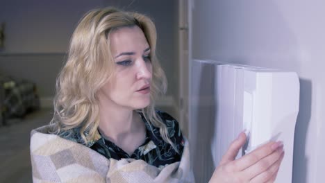 mujer con manta aumentando la temperatura del calentador eléctrico