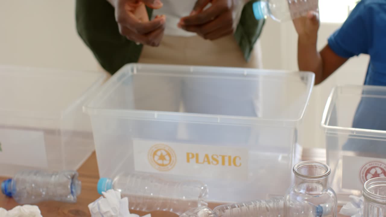 Hand lifting bottle, child, adult are sorting into plastic and glass bins on table for recycling