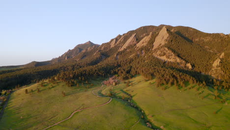 beautiful early morning sunrise shining warm light on colorado flatiron mountains, trees, and chautauqua trail for hiking near boulder with aerial drone flight