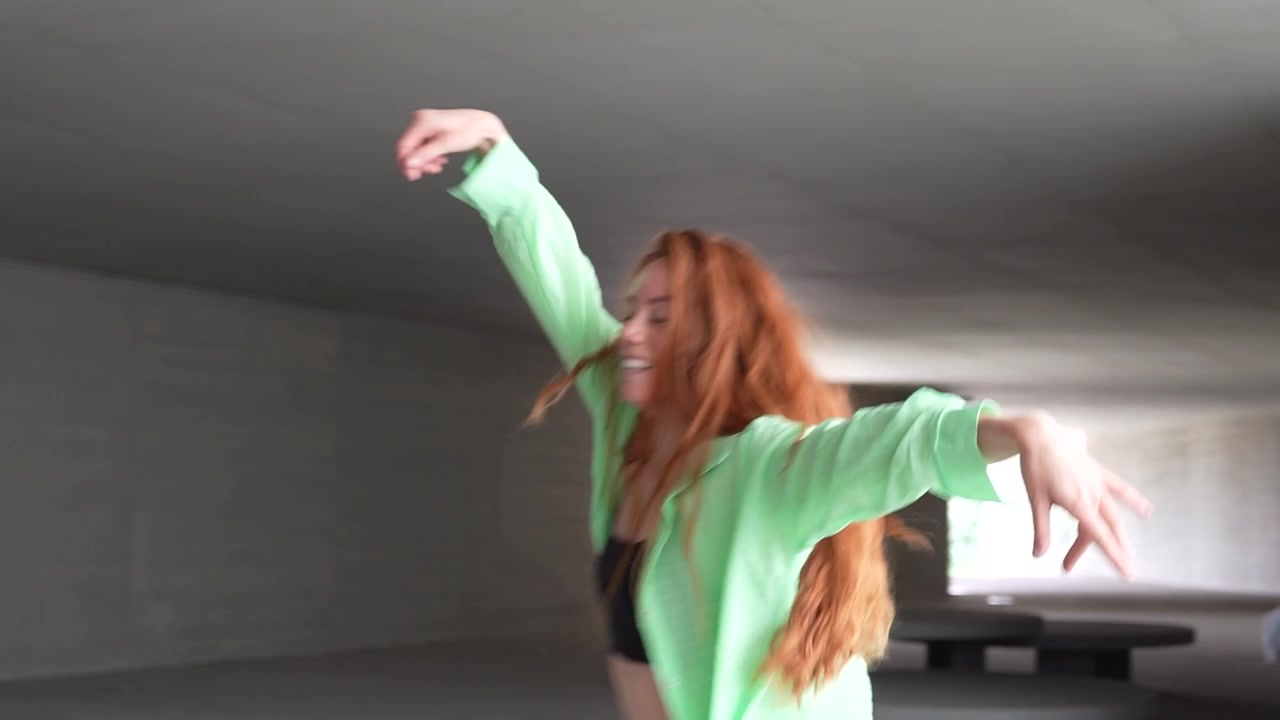A woman with vibrant red hair is dancing joyfully in a city tunnel expressing energy and happiness